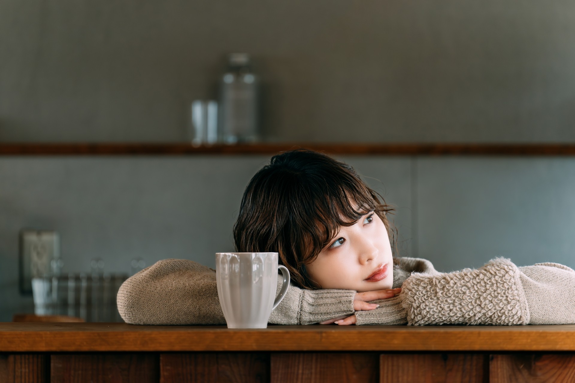 カフェのカウンターでマグカップを前に置き、顎を乗せて物思いにふける、婚活のデートや将来に悩む30代の女性